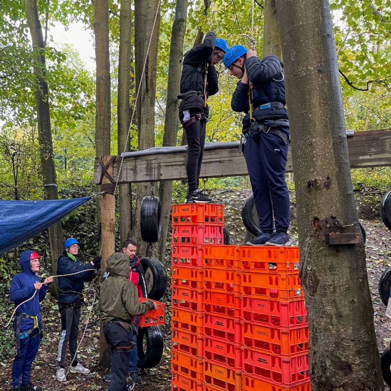 Young person balancing on stacked crates with a harness during a high-energy outdoor challenge.

