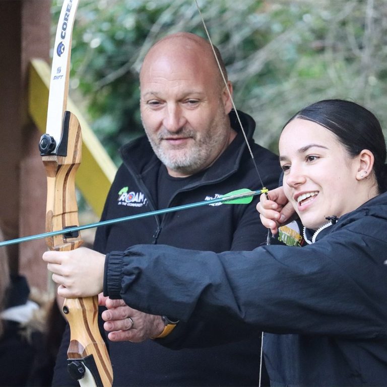 Alan supports a young person aiming a bow during an archery session at ROAM CIC.
