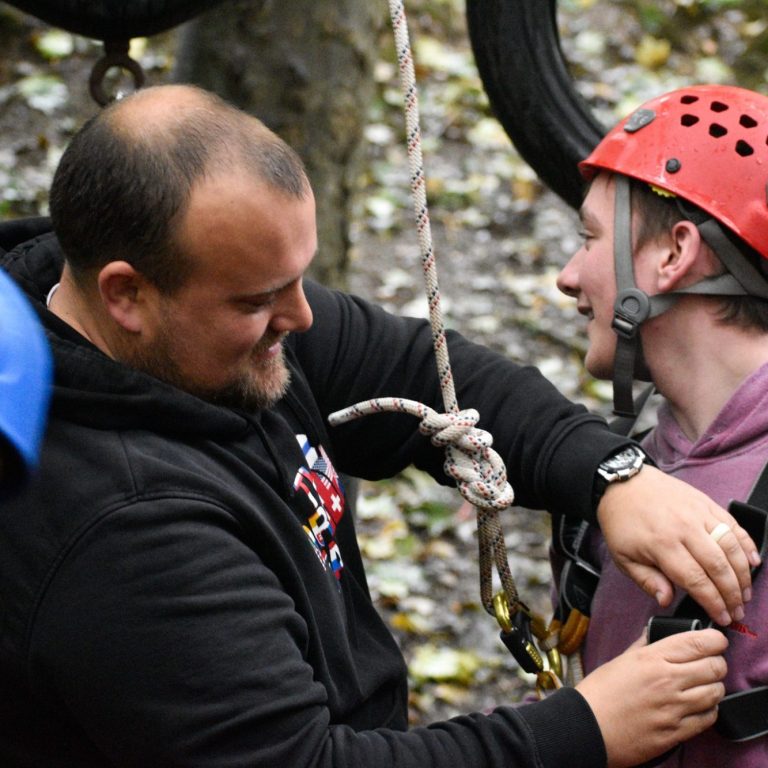 Adam helps a young person get ready with a helmet and harness before starting outdoor activities.
